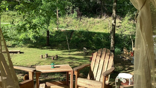 A wooden deck with a table and chairs, surrounded by a grassy area with trees.