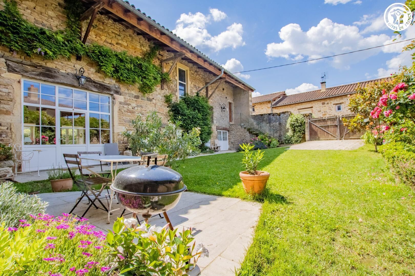 Uma casa de pedra com um pátio, churrasqueira e um jardim cheio de flores.