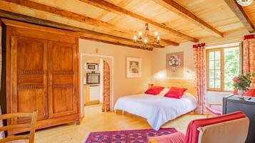 Um quarto aconchegante com teto de madeira, cama com roupa de cama vermelha e branca, um lustre e vista para o verde lá fora.