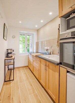 Cocina compacta con gabinetes de madera, horno integrado y ventana que proporciona luz natural.