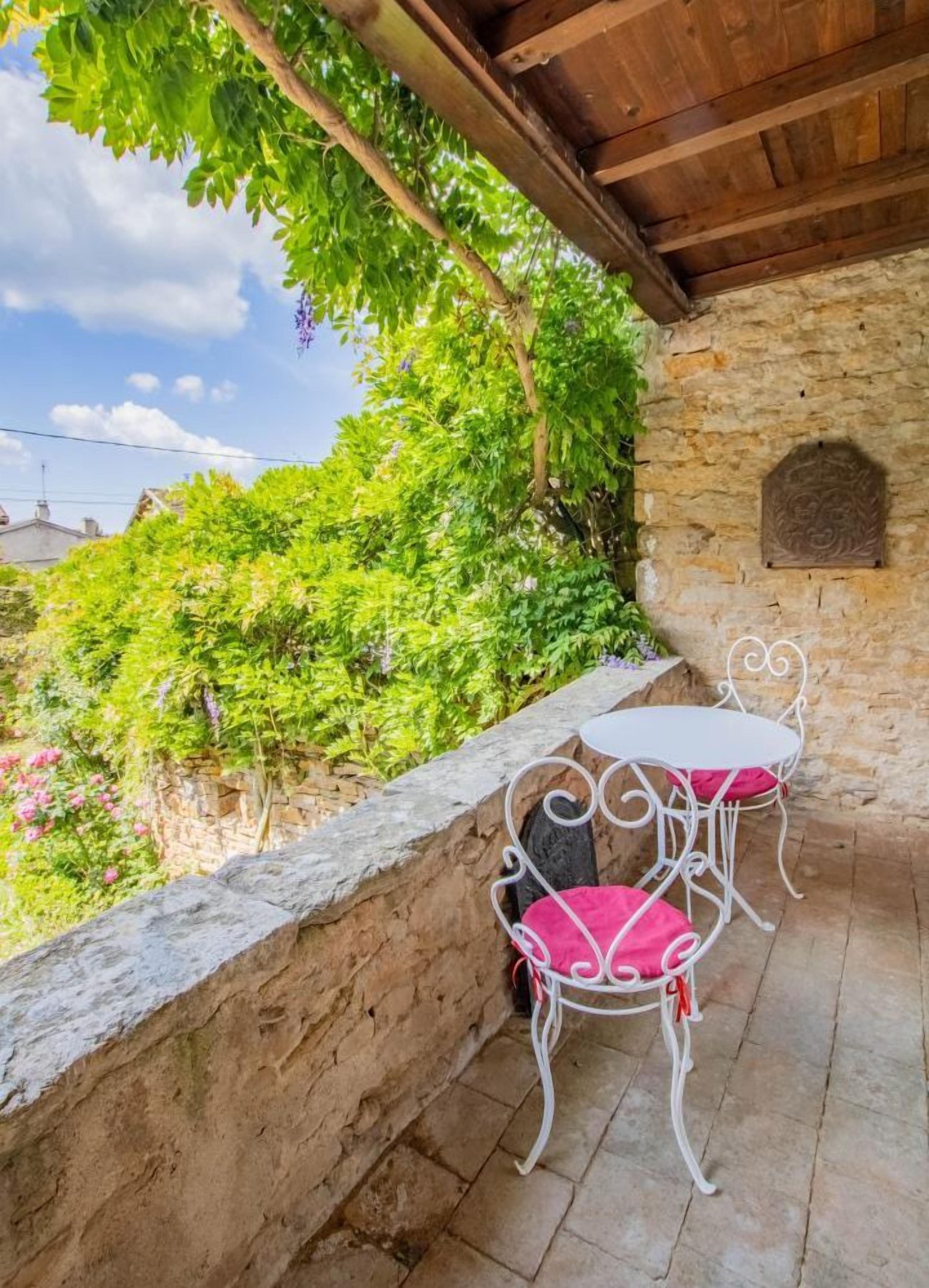 Pared de piedra con una mesa de metal blanco y dos sillas, techo de madera y vistas a la vegetación.