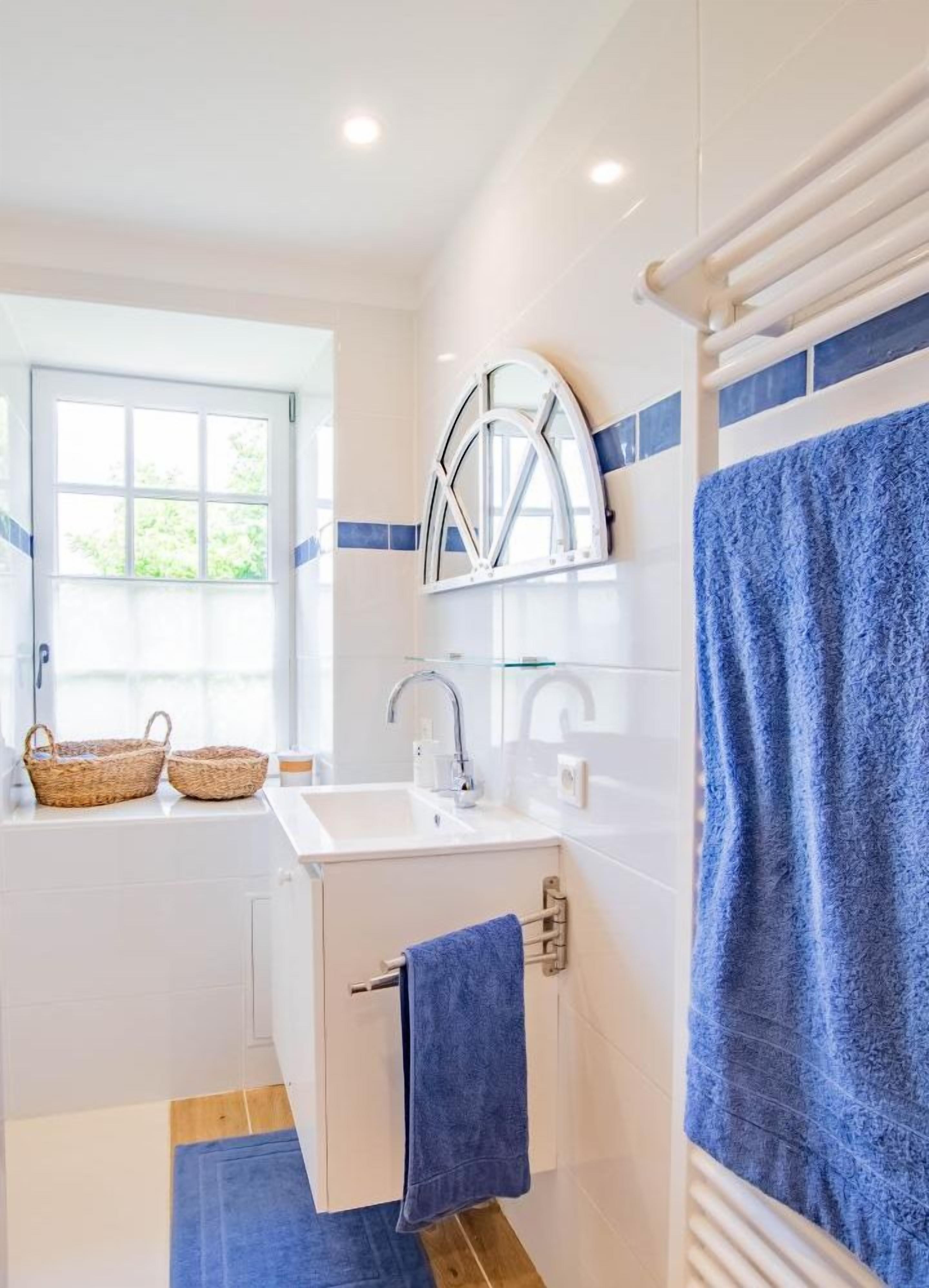 Une salle de bain avec un lavabo blanc, un miroir, un porte-serviettes et une fenêtre.