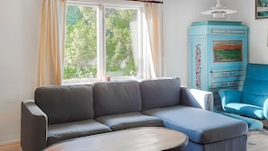 A living room with a grey sectional sofa, a small round table, a blue armchair, and a blue cabinet with floral designs. - Awesome home in Alsterbro with WiFi (Alsterbro)