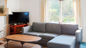 A living room with a grey sofa, a wooden coffee table, a TV on a red stand, and a window with curtains. - Awesome home in Alsterbro with WiFi (Alsterbro)