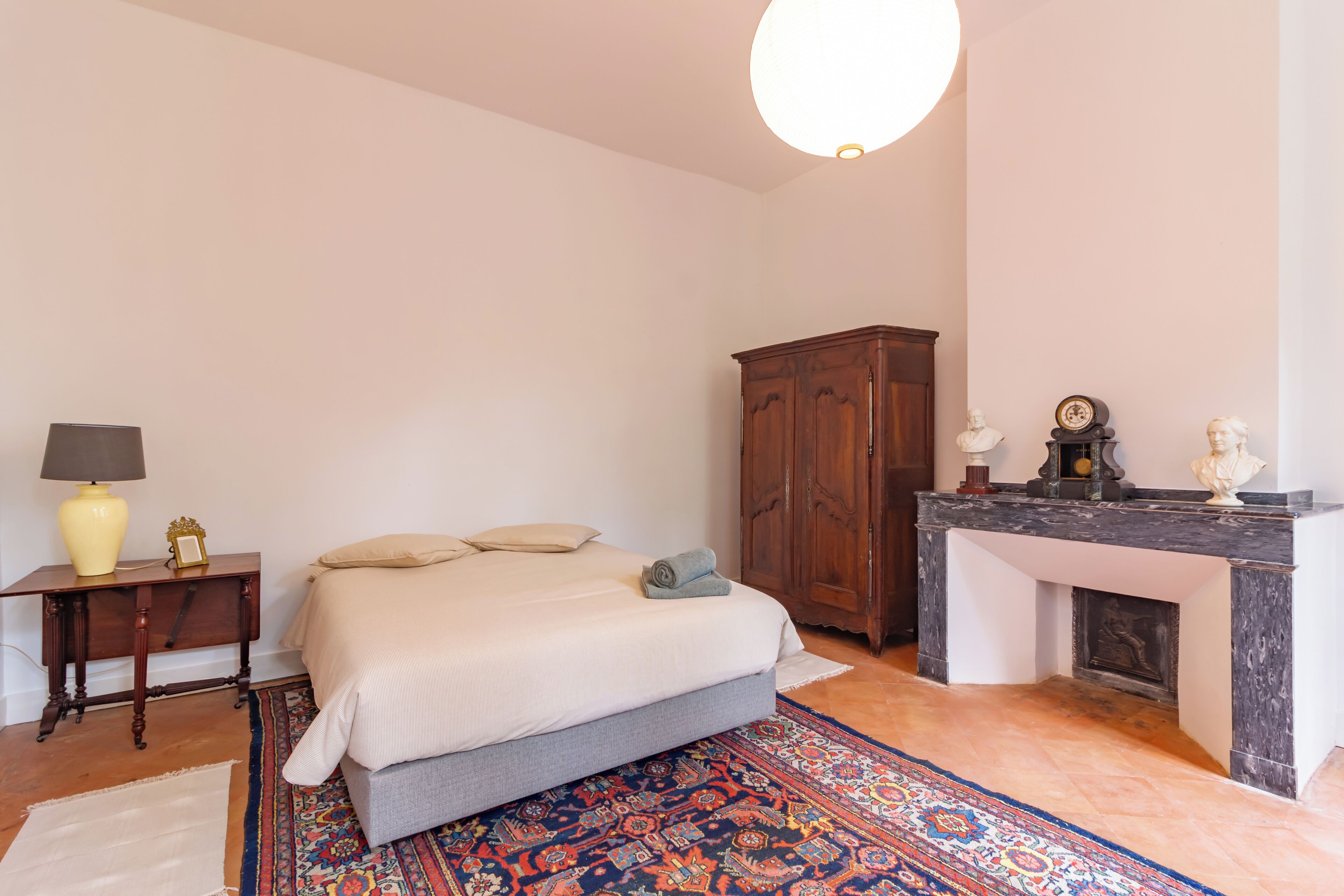 Een slaapkamer met een bed, een nachtkastje, een houten garderobe, een open haard en een vloerkleed.