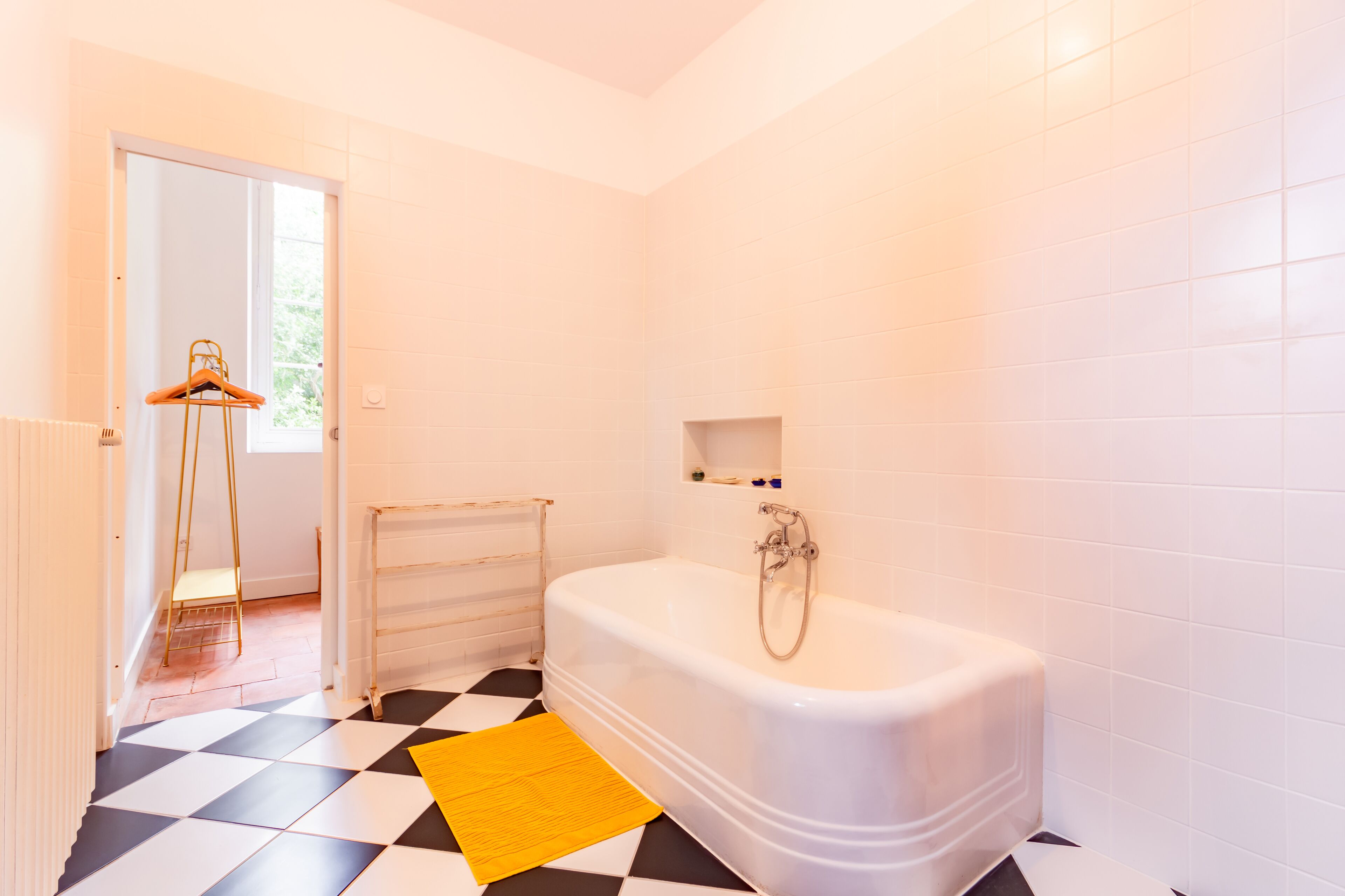 Un baño con una bañera blanca, un felpudo amarillo y un piso a cuadros.
