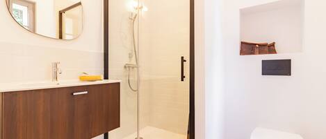 A modern bathroom with a glass-enclosed shower, a wooden vanity, and a white toilet.