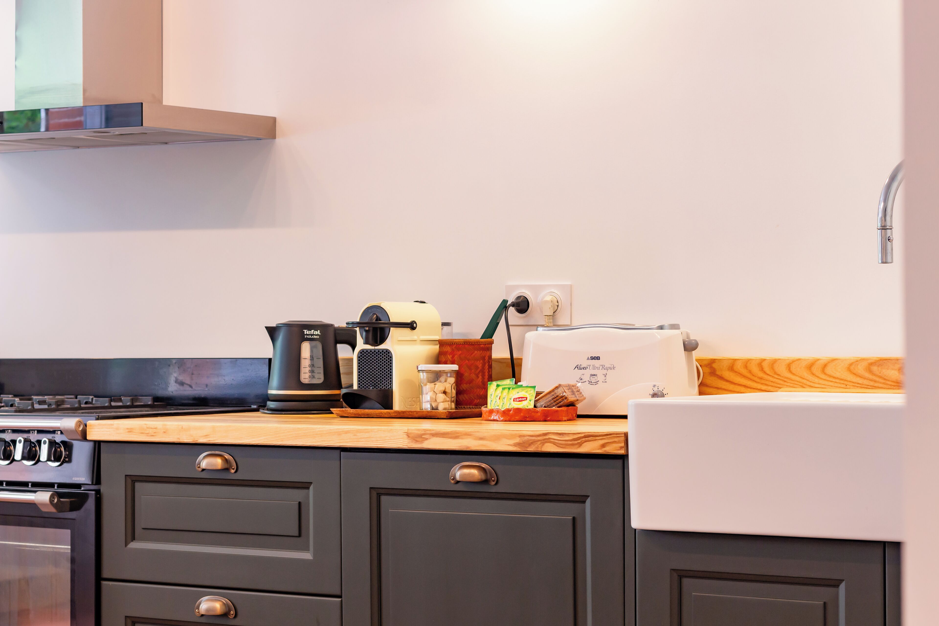 A kitchen with a stove, toaster, kettle, and a wooden countertop.