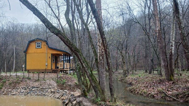 A yellow cabin with a porch, surrounded by a forest and a small stream. - "Ridge Haus" tiny cabin on the creek at Waldbaden (Athens)