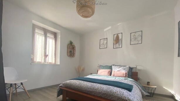Une chambre à coucher avec un lit en bois, une chaise blanche, une petite table et une fenêtre avec des rideaux.