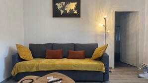 Un salon avec un canapé gris foncé, un plaid jaune moutarde et une carte du monde accrochée au mur.