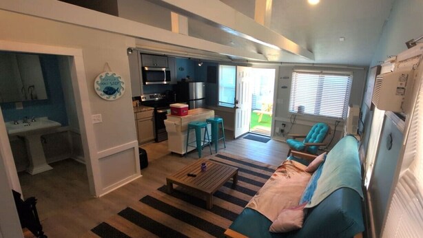 A compact living space with a kitchenette, a sofa, a coffee table, and a view of the outside. - Seaside Social - Steps to Wally's, Goat, L Street (Hampton)
