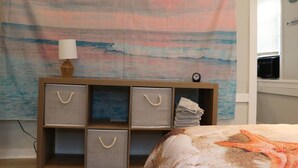 A bedroom with a beach-themed tapestry, a bedside table with a lamp, and a starfish decoration on the bed. - Seaside Social - Steps to Wally's, Goat, L Street (Hampton)
