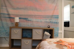 Una camera da letto con arazzo a tema spiaggia, un comodino con lampada e una decorazione a stella marina sul letto.