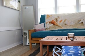 A room with a bed, a table with a remote, a window, and a door.