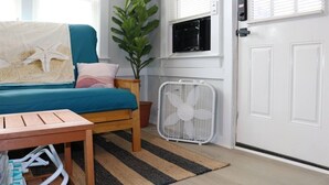A bedroom with a bed, a bedside table, a fan, a potted plant, and a window with blinds. - Seaside Social Deluxe - Steps to Wally's, Goat (Hampton)