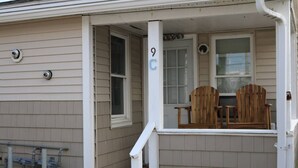 A house with a porch, two wooden chairs, a small table, and a number '9C' on the door. - Seaside Social Deluxe - Steps to Wally's, Goat (Hampton)