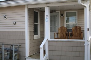 A house with a porch, two wooden chairs, a small table, and a number '9C' on the door.