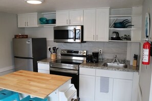A compact kitchen with white cabinets, a stainless steel refrigerator, a microwave, an oven, and a coffee maker.