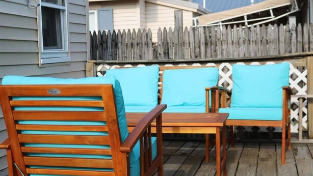 A wooden deck with two chairs and a table, a wooden fence, and a house in the background. - Seaside Social Deluxe - Steps to Wally's, Goat (Hampton)