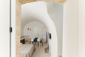Een kleine keuken met witte kastjes, een eettafel met stoelen, en een kleine koelkast.