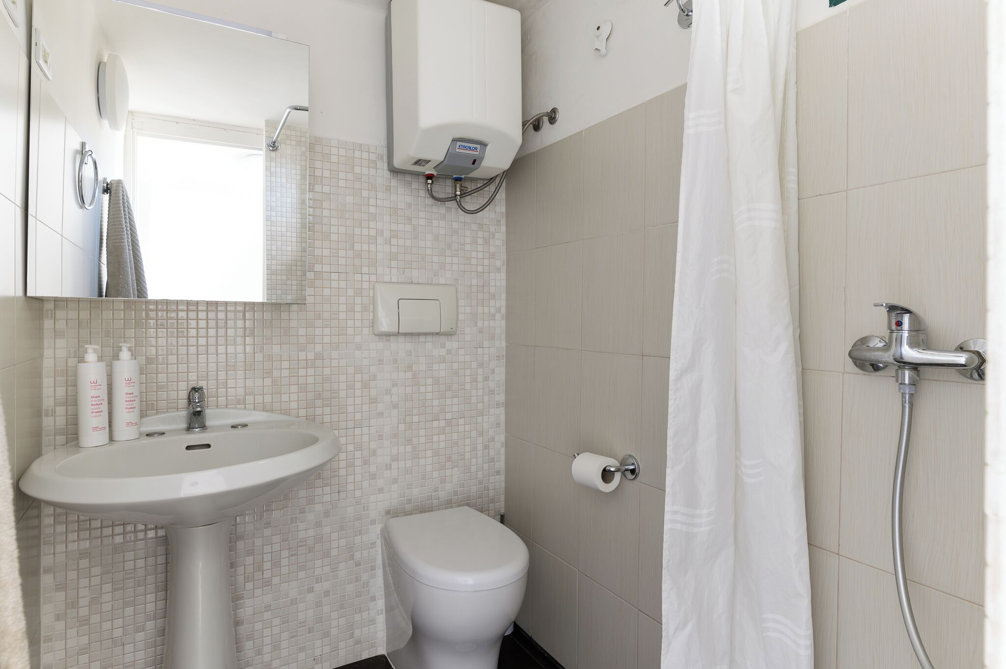 Une salle de bain avec un lavabo, des toilettes et une douche, le tout de couleur blanche.