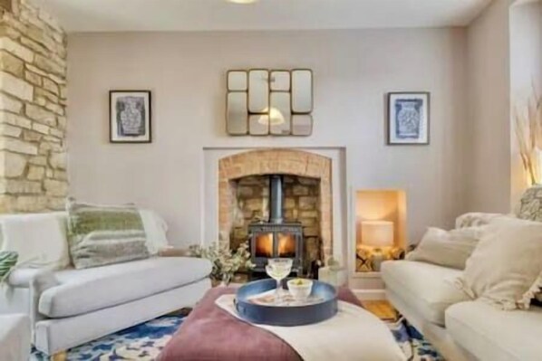 A cozy living room with a stone wall, a fireplace, and two sofas. - Luxury Boutique Cotswold Cottage with Hot Tub! (Winchcombe)