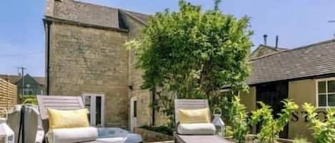 A stone building with a garden area featuring two lounge chairs and a small table.