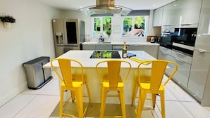 A modern kitchen with a central island, yellow chairs, stainless steel appliances, and a view of greenery outside. - Stunning cotswold, period country house, hot tub, great for extended family (Gloucestershire)