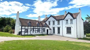 A traditional Tudor-style building with multiple chimneys, a prominent white facade, and a symmetrical design. - Stunning cotswold, period country house, hot tub, great for extended family (Gloucestershire)