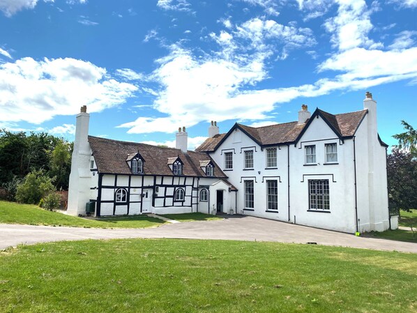 A traditional Tudor-style building with multiple chimneys, a prominent white facade, and a symmetrical design. - Stunning cotswold, period country house, hot tub, great for extended family (Gloucestershire)