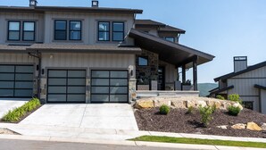Une maison moderne à deux étages, dotée d’un garage, d’une façade en pierre et d’un porche abrité.