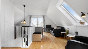 A modern loft apartment with a high ceiling, a sloped roof, a dining area, a living room with a sofa and a TV, and a kitchen area with a balcony. - Cozy home in Farsø with WiFi (Farsø)