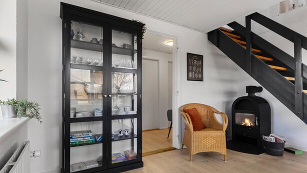 A living room with a black cabinet, a wicker chair, a fireplace, and a staircase. - Cozy home in Farsø with WiFi (Farsø)