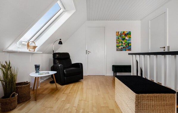 A small, bright room with a sloped ceiling, a black leather chair, a small table, a wicker basket, and a colorful abstract painting on the wall. - Cozy home in Farsø with WiFi (Farsø)
