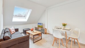 Una sala de estar moderna con un sofá, una mesa de centro, una mesa de comedor con sillas, un televisor y un tragaluz.