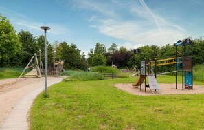 Explore a playground with a slide, climbing frames, and a swing set, set amidst lush greenery.