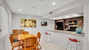 A modern kitchen with a dining area, featuring a wooden table and chairs, a kitchen island with stools, and a large abstract painting on the wall. - Palm Springs 2-bedroom, 2 Bath Ground Floor condo. Garage. Pool, Hot Tub, Tennis (Palm Springs)
