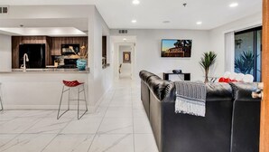 A modern living room with a black leather sofa, a red chair, and a kitchen area with dark wooden cabinets and a black refrigerator. - Palm Springs 2-bedroom, 2 Bath Ground Floor condo. Garage. Pool, Hot Tub, Tennis (Palm Springs)