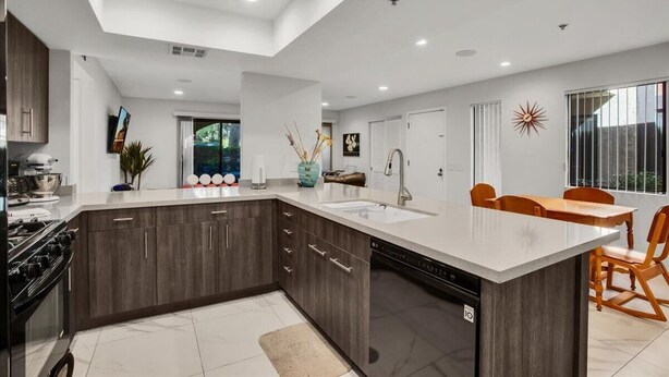 A modern kitchen with dark wood cabinets, a large island with a sink, and a dining area with a table and chairs. - Palm Springs 2-bedroom, 2 Bath Ground Floor condo. Garage. Pool, Hot Tub, Tennis (Palm Springs)