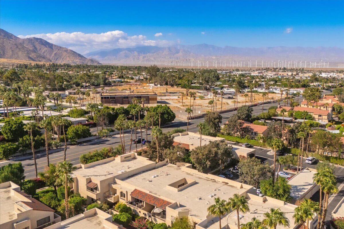 A residential area with houses, palm trees, and a distant view of wind turbines.