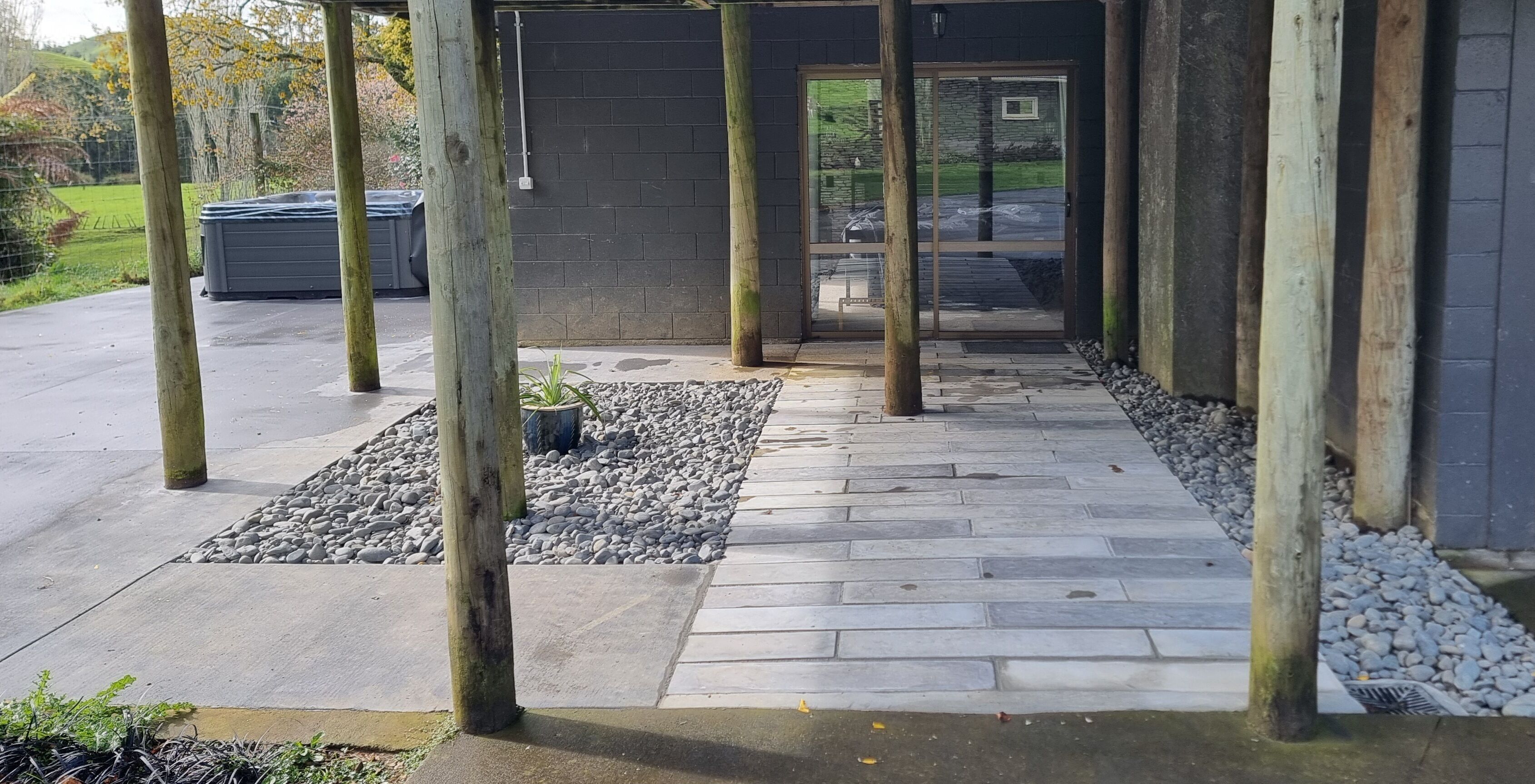 A covered outdoor area with stone flooring and wooden posts, leading to a glass door.
