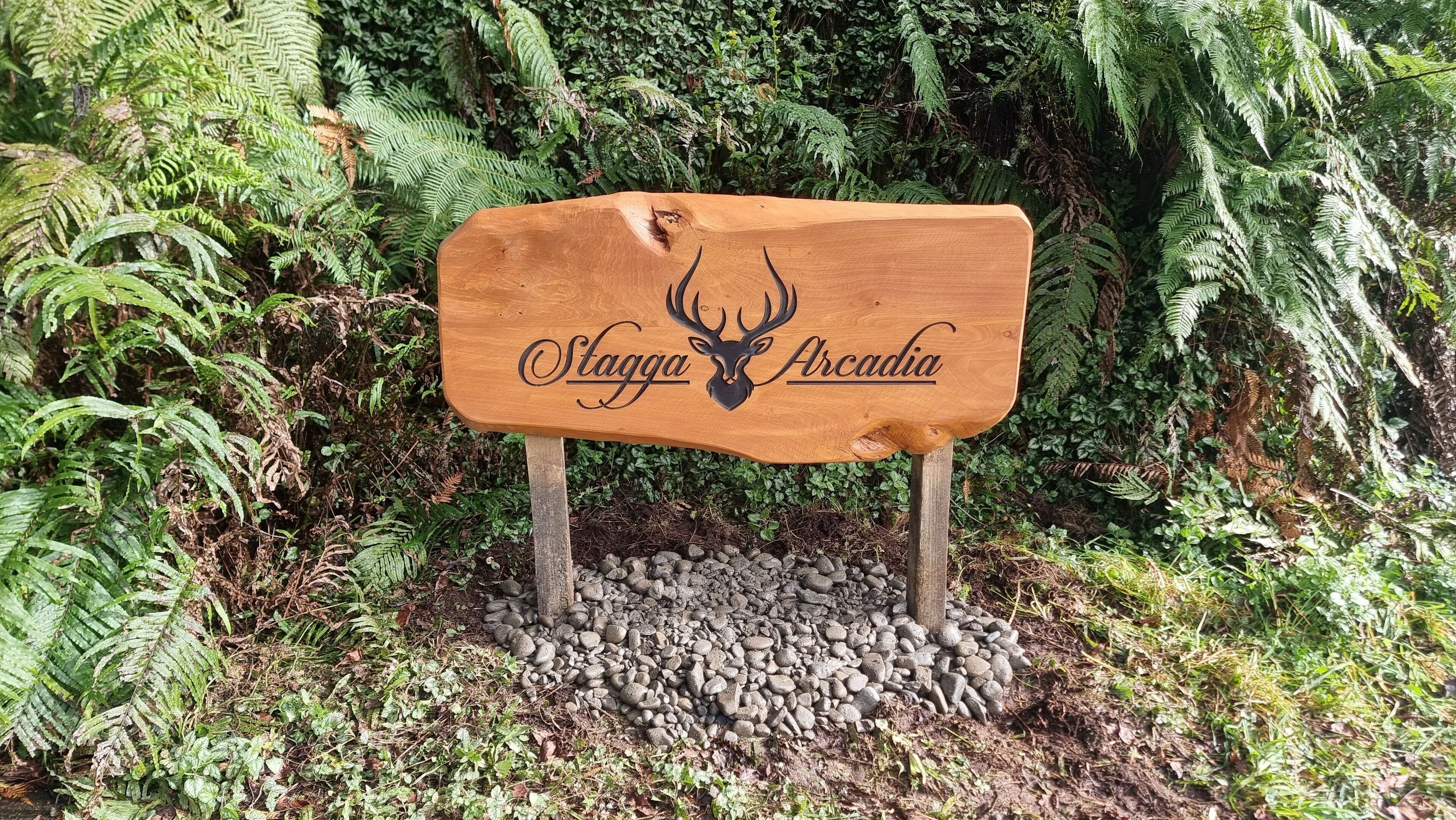 Ein Holzschild mit einem Hirschkopf und dem Schriftzug 'Slagga Arcadia' in einer Waldlandschaft.