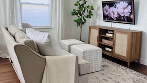 Una sala de estar moderna con un sofá, un reposapiés, un televisor y una planta.