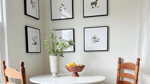 Un comedor con dos sillas de madera, una mesa blanca y un jarrón con una planta.