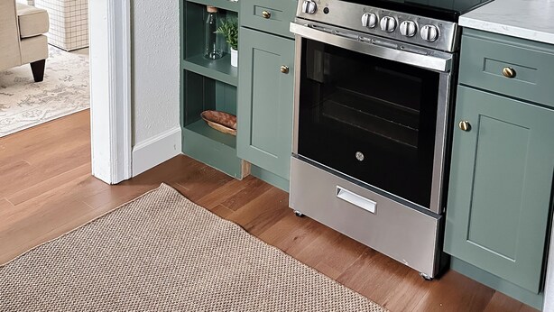 Una cocina con armarios verdes, horno de acero inoxidable y encimera blanca.