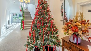 Eine prachtvolle Eingangshalle mit geschmücktem Weihnachtsbaum, einer Treppe und einem Spiegel, der den Baum reflektiert.