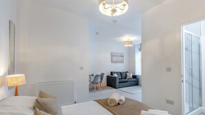 Ein modernes Hotelzimmer mit einem großen Bett, einer Sitzecke mit Sofa und Sesseln, einer Glastür, die auf einen Balkon führt, und einer Deckenleuchte.