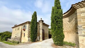 Un edificio de piedra con un camino de grava, una ventana con contraventanas y un letrero que dice "La Posada".
