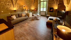 Una habitación acogedora con paredes de piedra, suelo de madera, un sofá, una mesa de comedor con sillas y una cama con una lámpara.